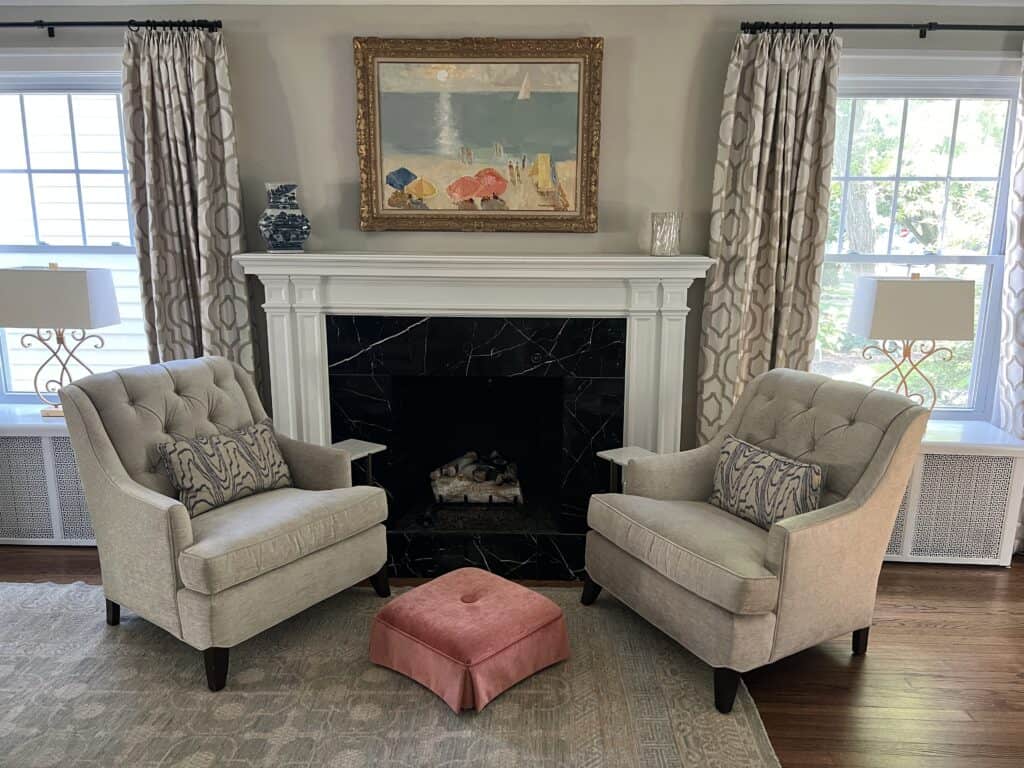 Two chairs flanking a fireplace with a painting of a beach scene above the mantle