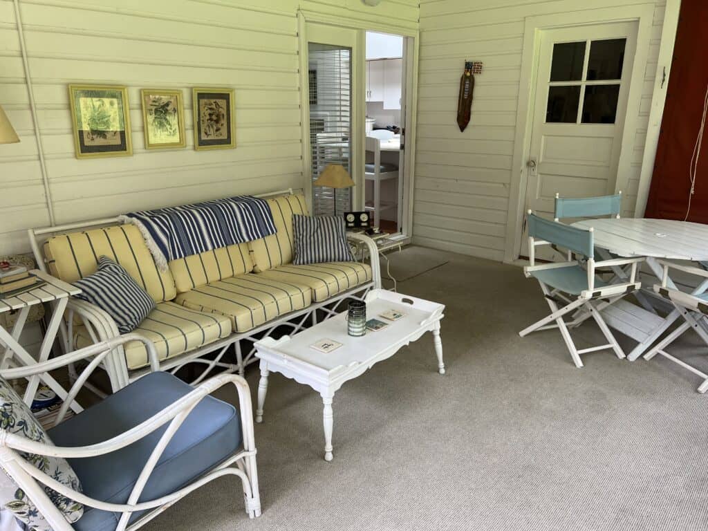 Screened porch with rattan furniture styled in variations of yellow and blue fabric. 