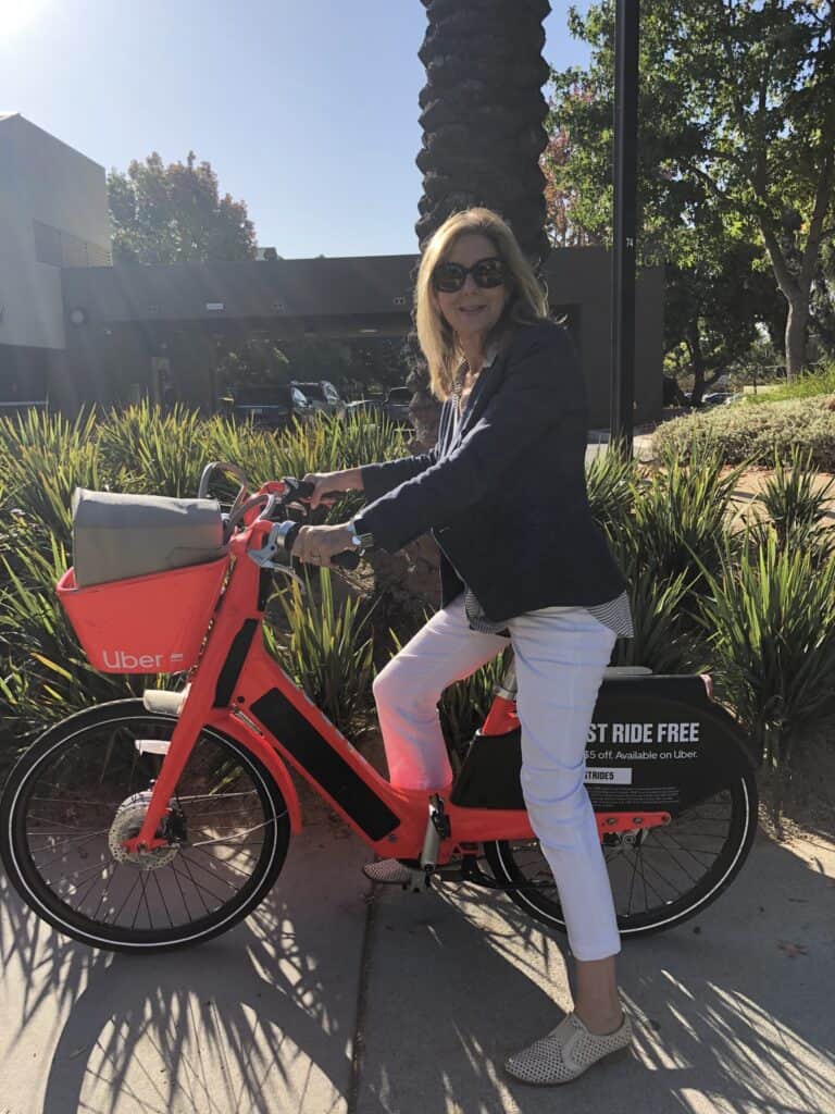 Woman riding an Uber electric bike to a work meeting in Santa Monica, CA.  Work tote is in the bike basket. 