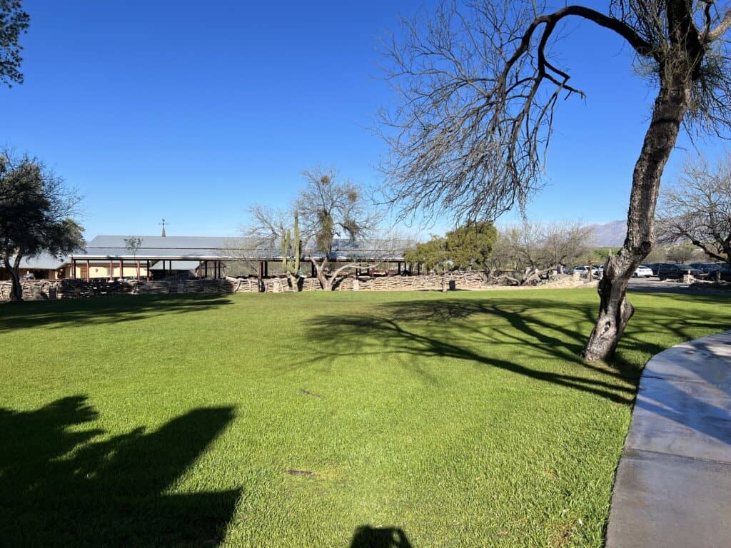 View of a green lawn with horse corrals in the distance, with mountains beyond.