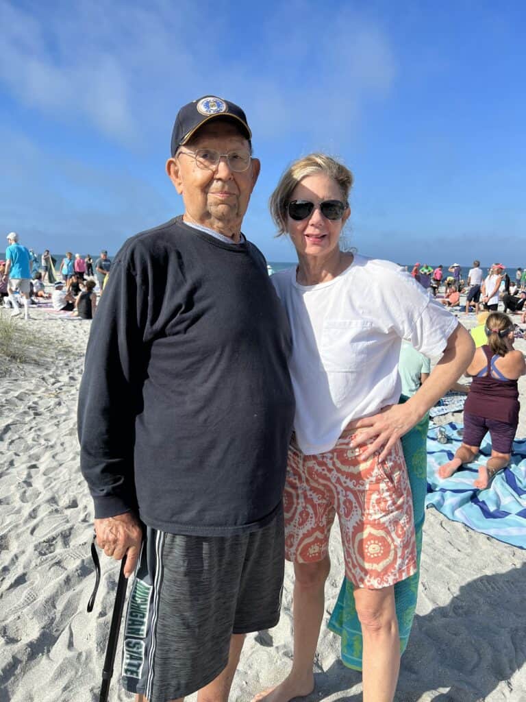 Woman and her father standing on the beach after completing a yoga class.