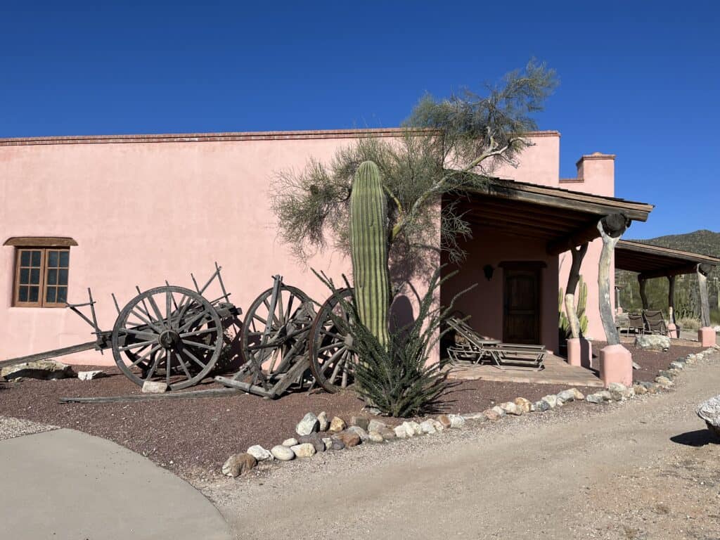 Photo of a pink stucco building with old wagon wheels leaning against it. 