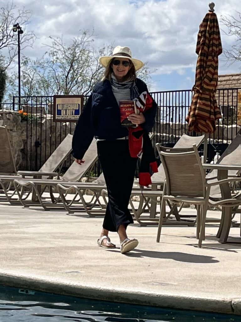 Woman walking by a pool with a coat and hat on. 