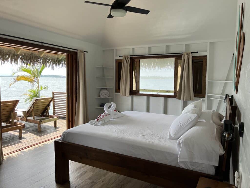 Photo of main bedroom with deck and lounge chairs just outside in an affordable overwater bungalow. 