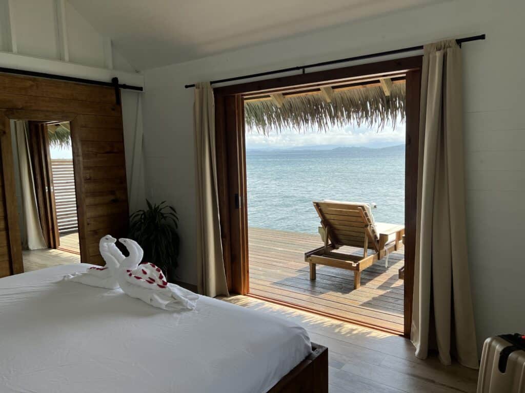 Another view of the ocean, deck and lounge chairs from the main bedroom of an affordable overwater bungalow.