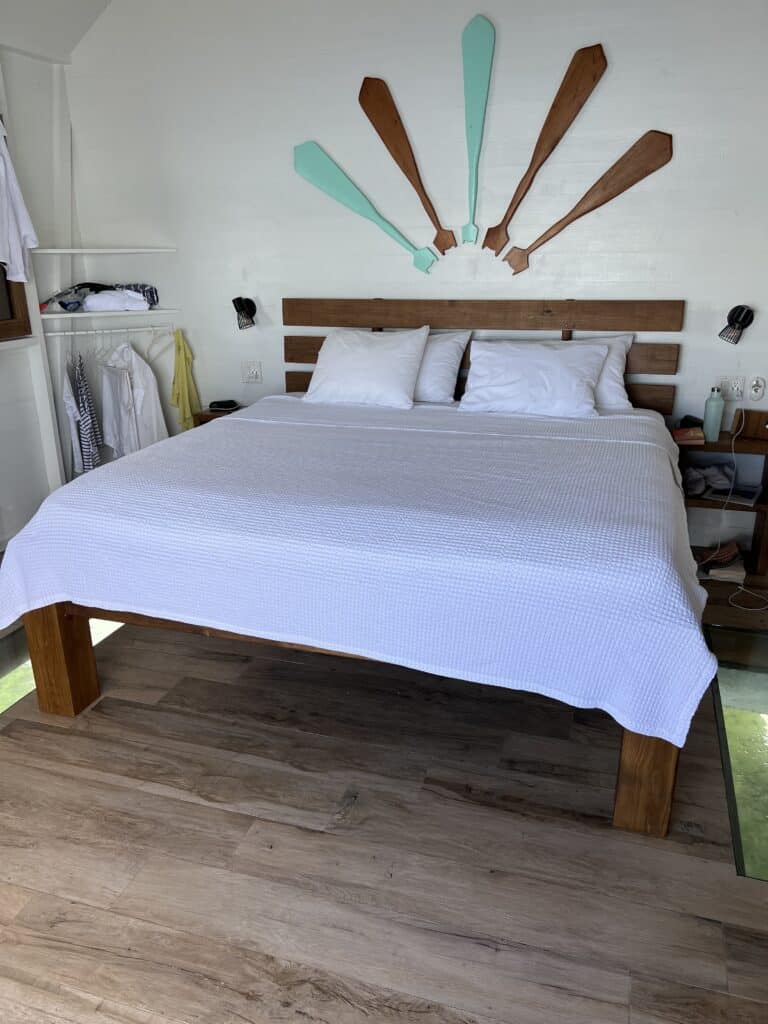 Photo of queen size bed in an affordable overwater bungalow with a glass bottom floor on either side.