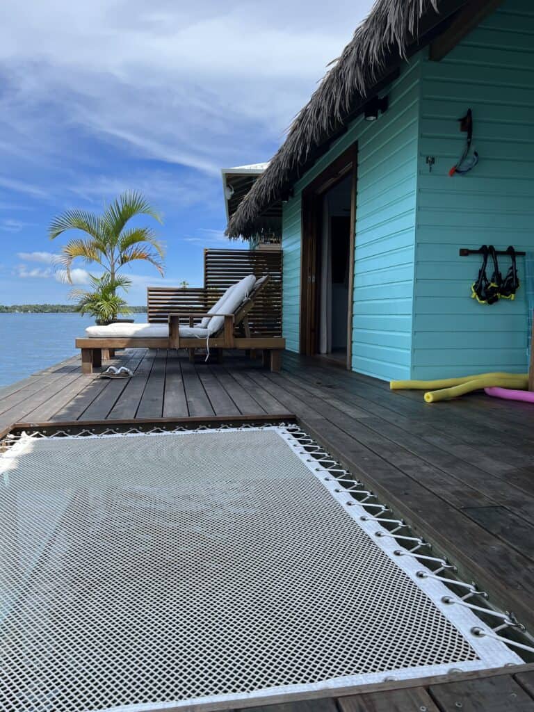 Photo of a deck with a catamaran net, lounge chairs and the ocean beyond.
