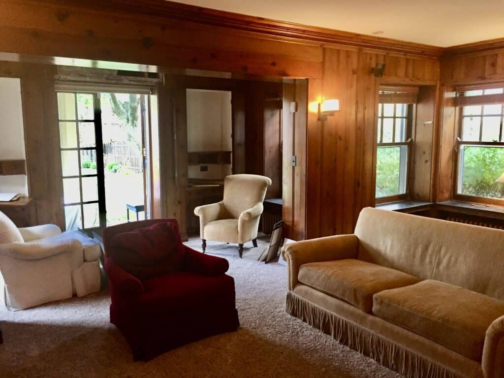 Before, a view of the dark, moody paneled family room with a set of small french doors and built-in desks.