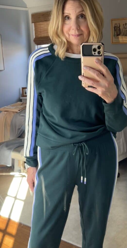 Woman, trying to improve her loungewear game, in a two-piece matching track set in green with white and blue stripes down the side. 