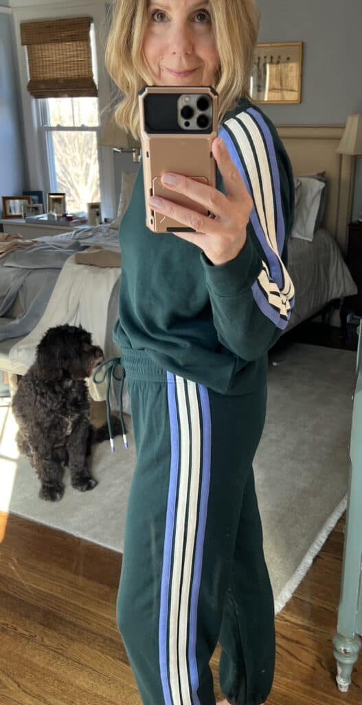 Side view of a woman in a green track suit with blue and white stripes down the side. 