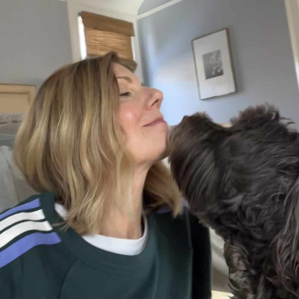 Close up of woman with her brown dog kissing her chin. 