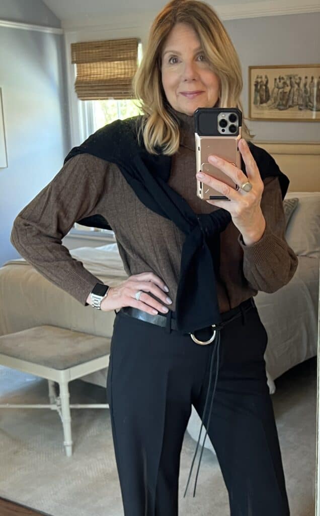 Photo of a woman in black slacks, brown cashmere turtleneck and black sweater draped over her shoulders. 