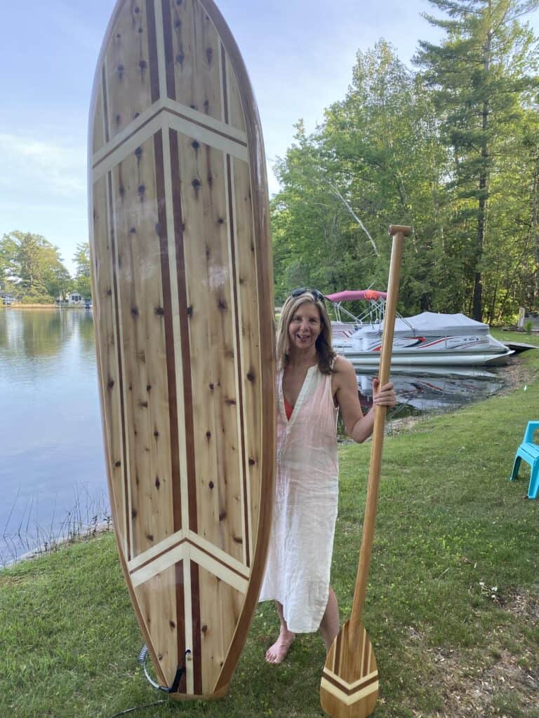 Woman standing with her favorite water toy for the lake, a custom wood paddleboard.