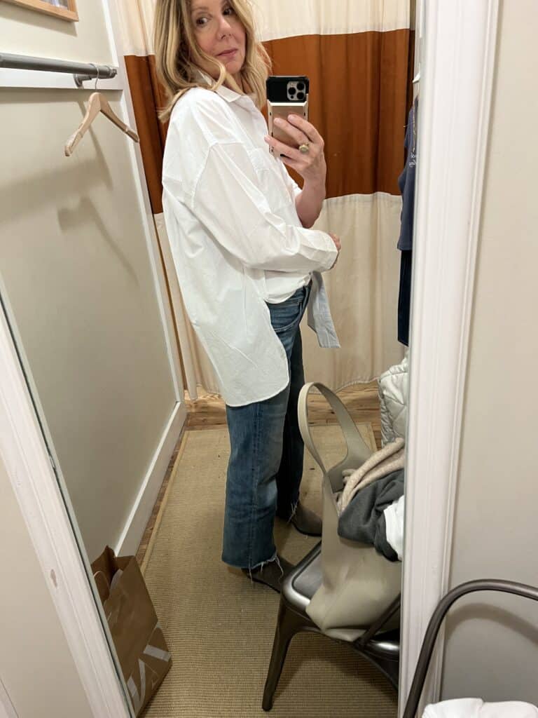 Sideview of the woman standing in a dressing room, trying on a shirt 