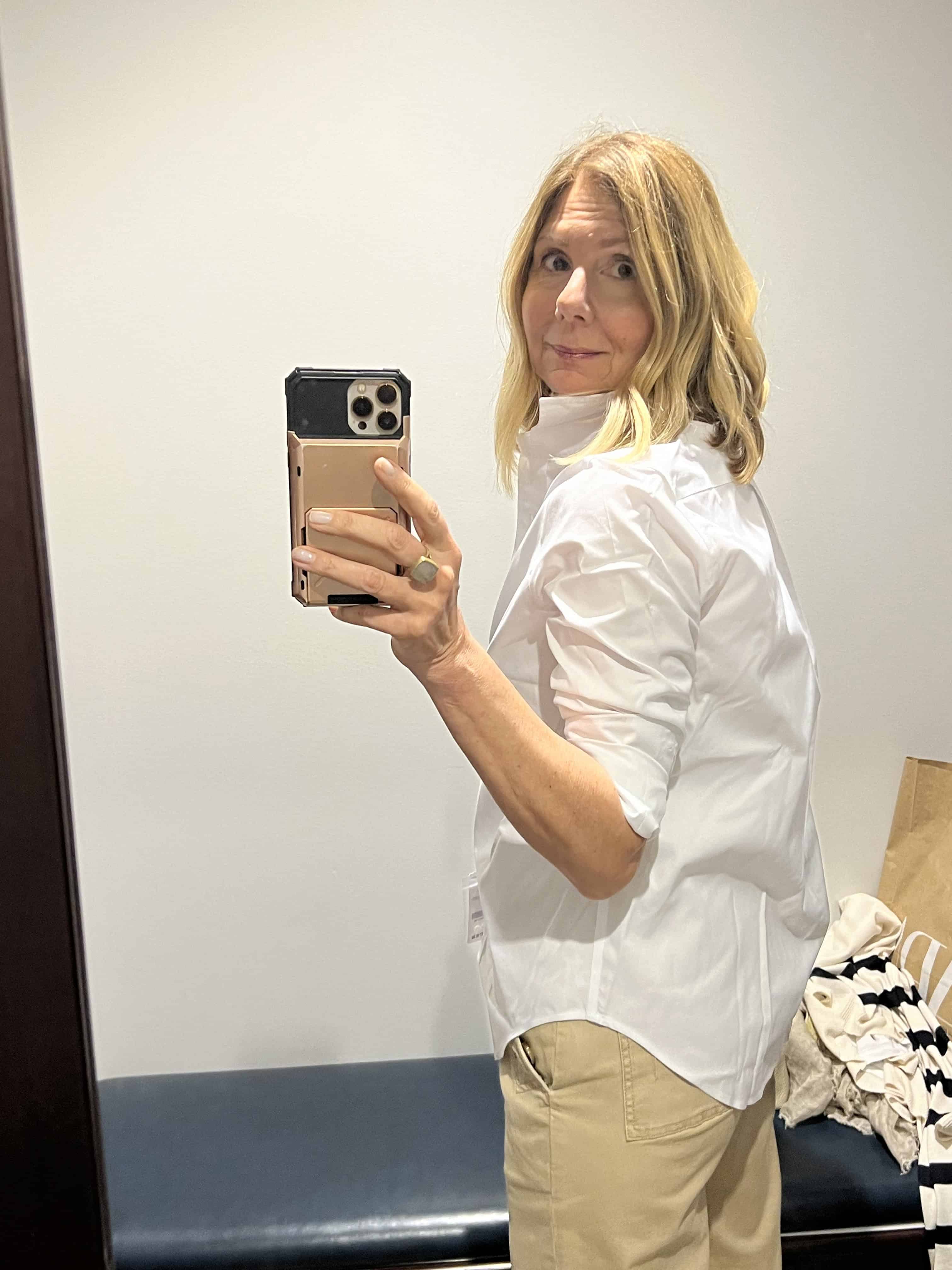 Side view of a woman trying on a Brooks Brothers white button-down shirt. 