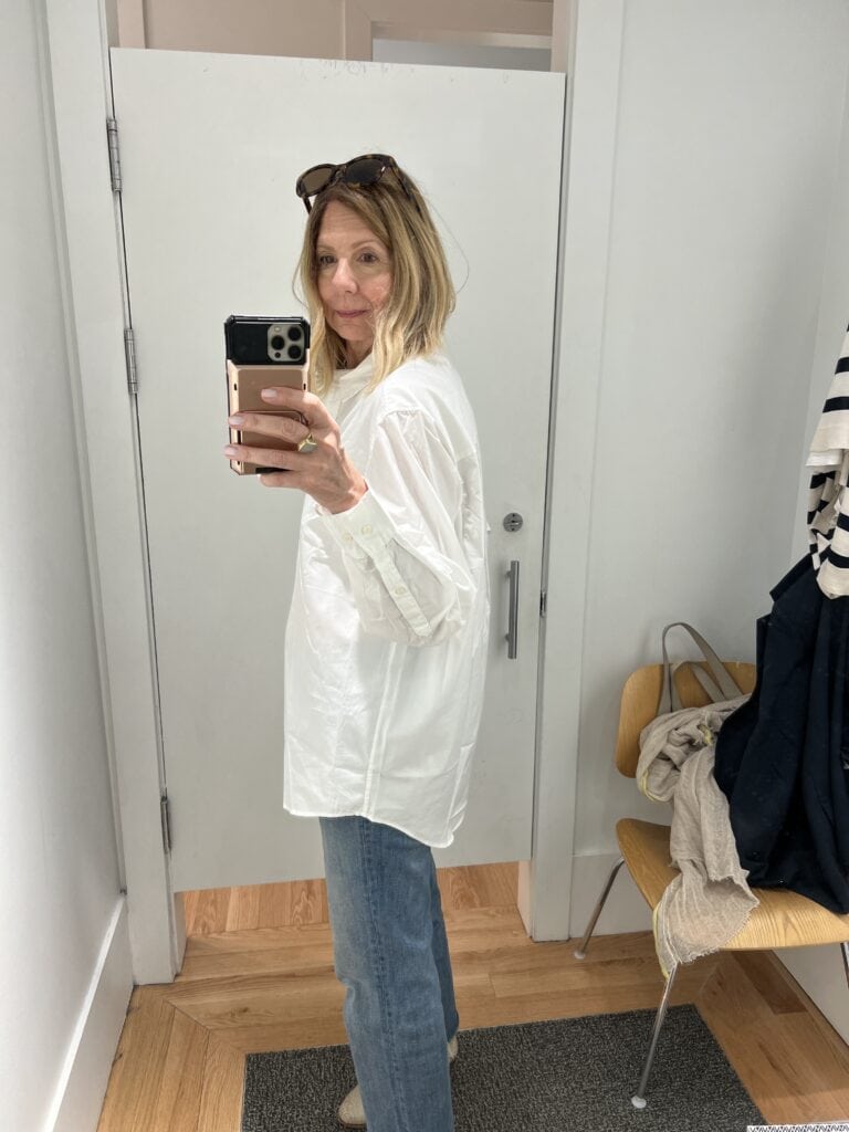 Woman in a Gap dressing room trying on an oversized white button down shirt. 