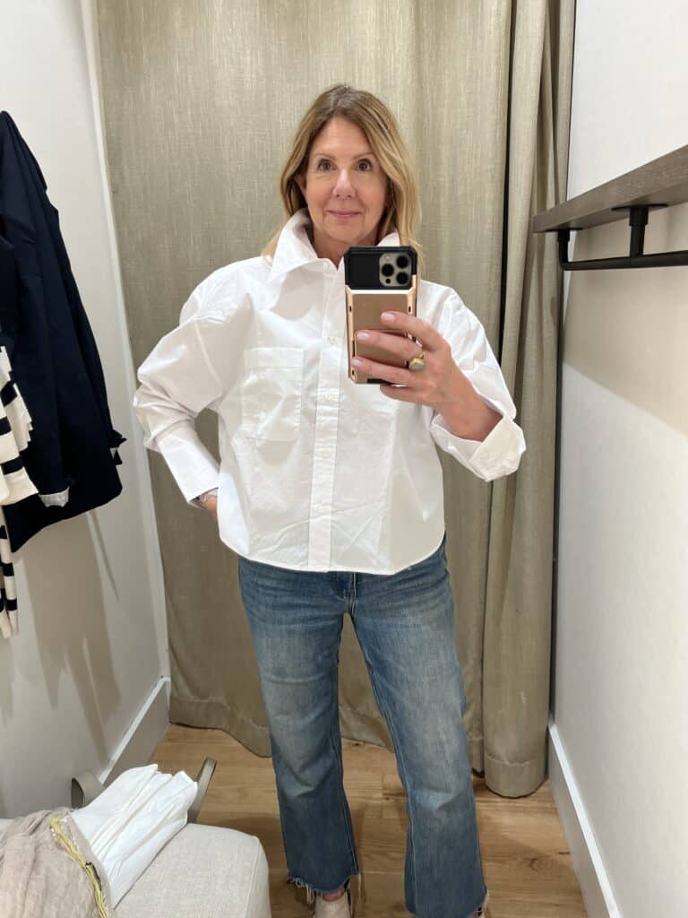 Woman in a Banana Republic dressing room trying on a white, cropped shirt. 