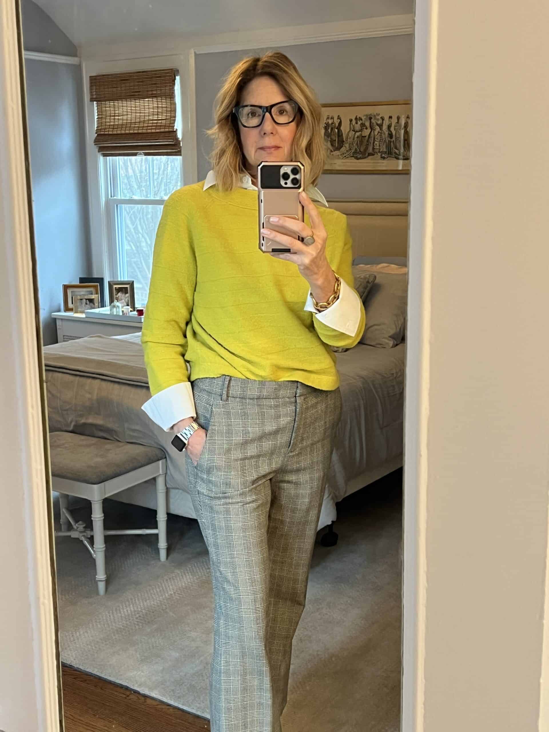 Woman in a white button-down shirt with a yellow sweater over with the cuffs folded back.