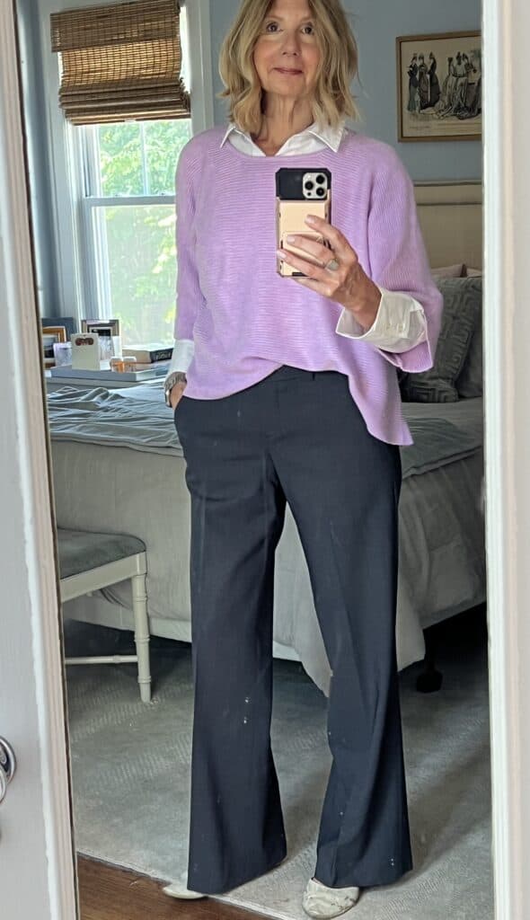 Woman in grey slacks and a white button-down shirt with a lavender sweater layered over the shirt. 