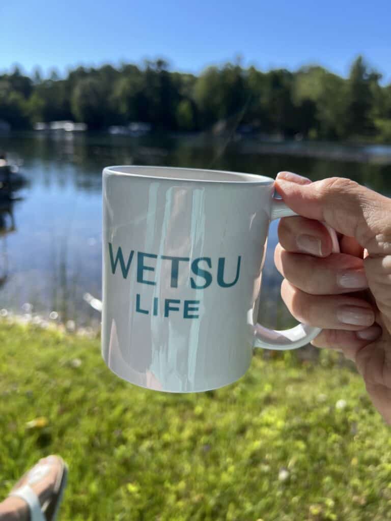 Photo of a hand holding the WETSU Life mug with water in the background. 