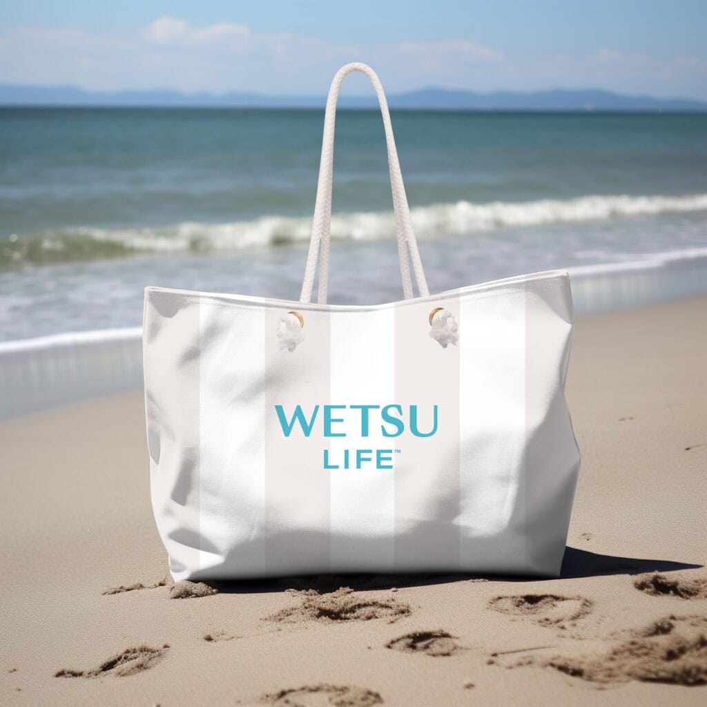 The WETSU Life cabana stripe tote bag sitting on a beach.