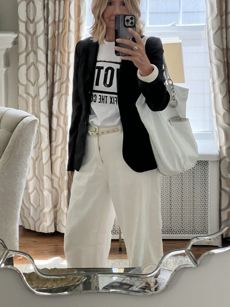 Woman in white barrel leg pants with a black blazer and graphic tee shirt. 