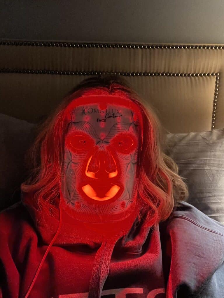 Woman using the Omnilux Red Light Therapy mask. 