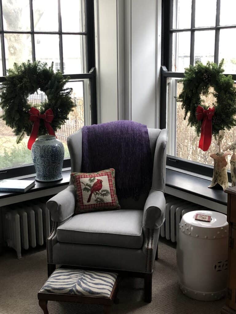 Photo of a chair surrounded by two windows adorned with wreaths part of simple Christmas Decor. 