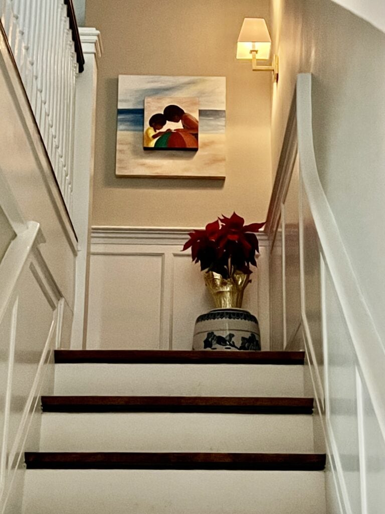 Photo of a poinsettia placed atop a  Chinese pottery stool on a stair landing. 