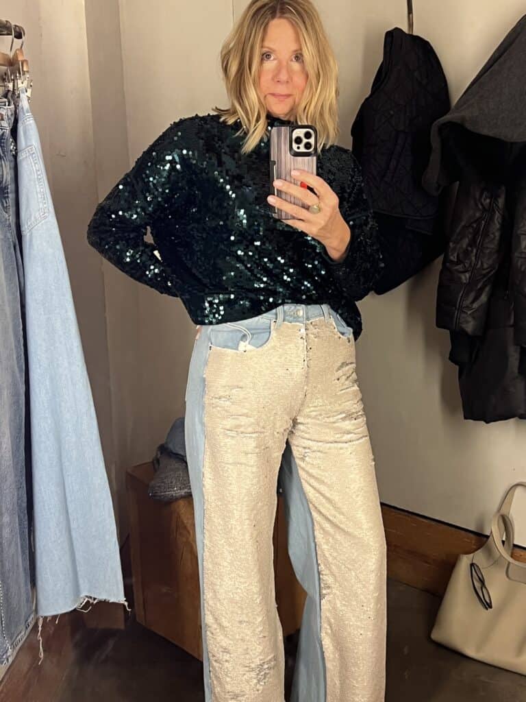 Woman trying on a green sequin top and sequin jeans for affordable holiday outfits. 