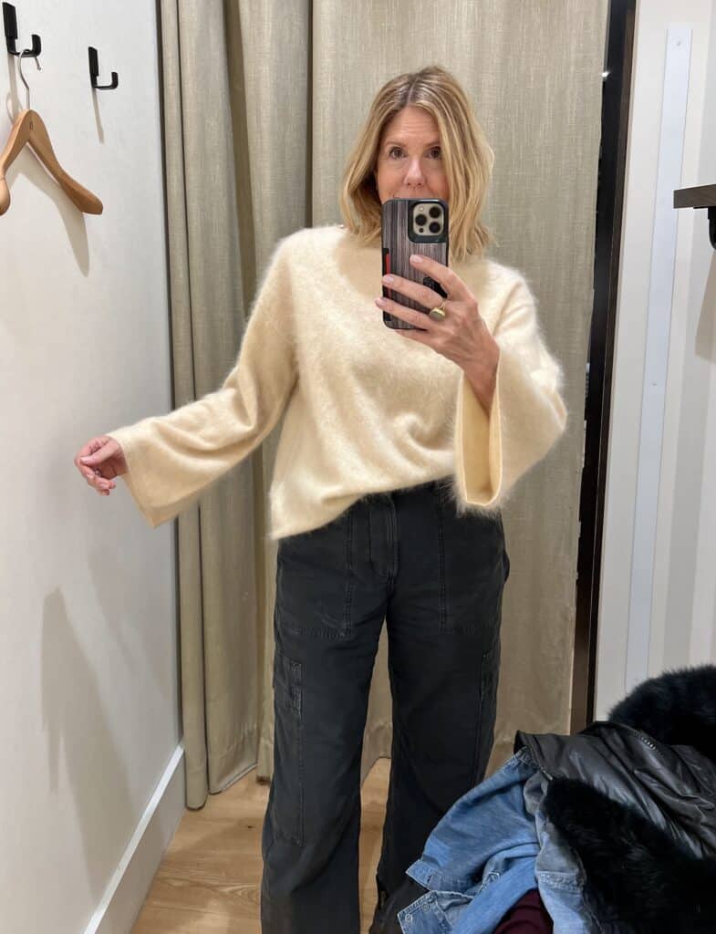 Woman trying on a cream-colored brushed cashmere flare sleeve sweater. 