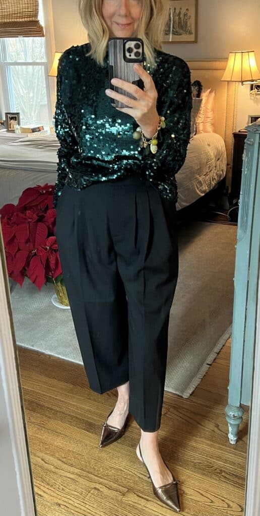 Woman in a green sequin sweater with black pants and gold kitten heel pumps. 