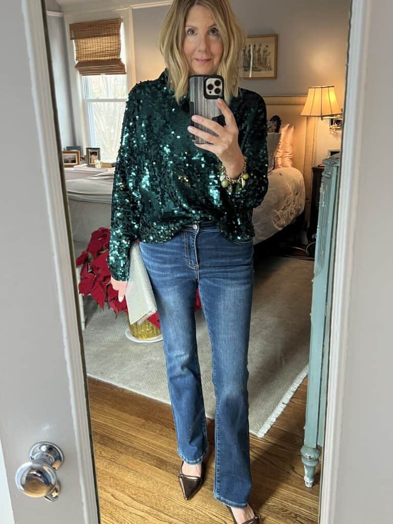 Woman putting together an affordable holiday outfit in flare jeans and a green sequin top 