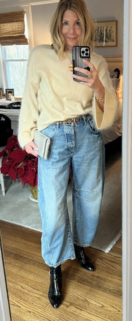 Woman in barrel jeans, brushed cashmere sweater and boots as an affordable holiday outfit. 