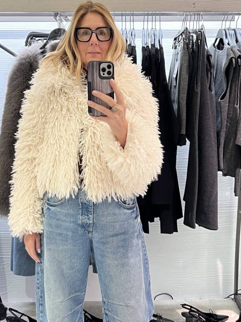 Woman trying on a cream fuzzy faux fur jacket. 